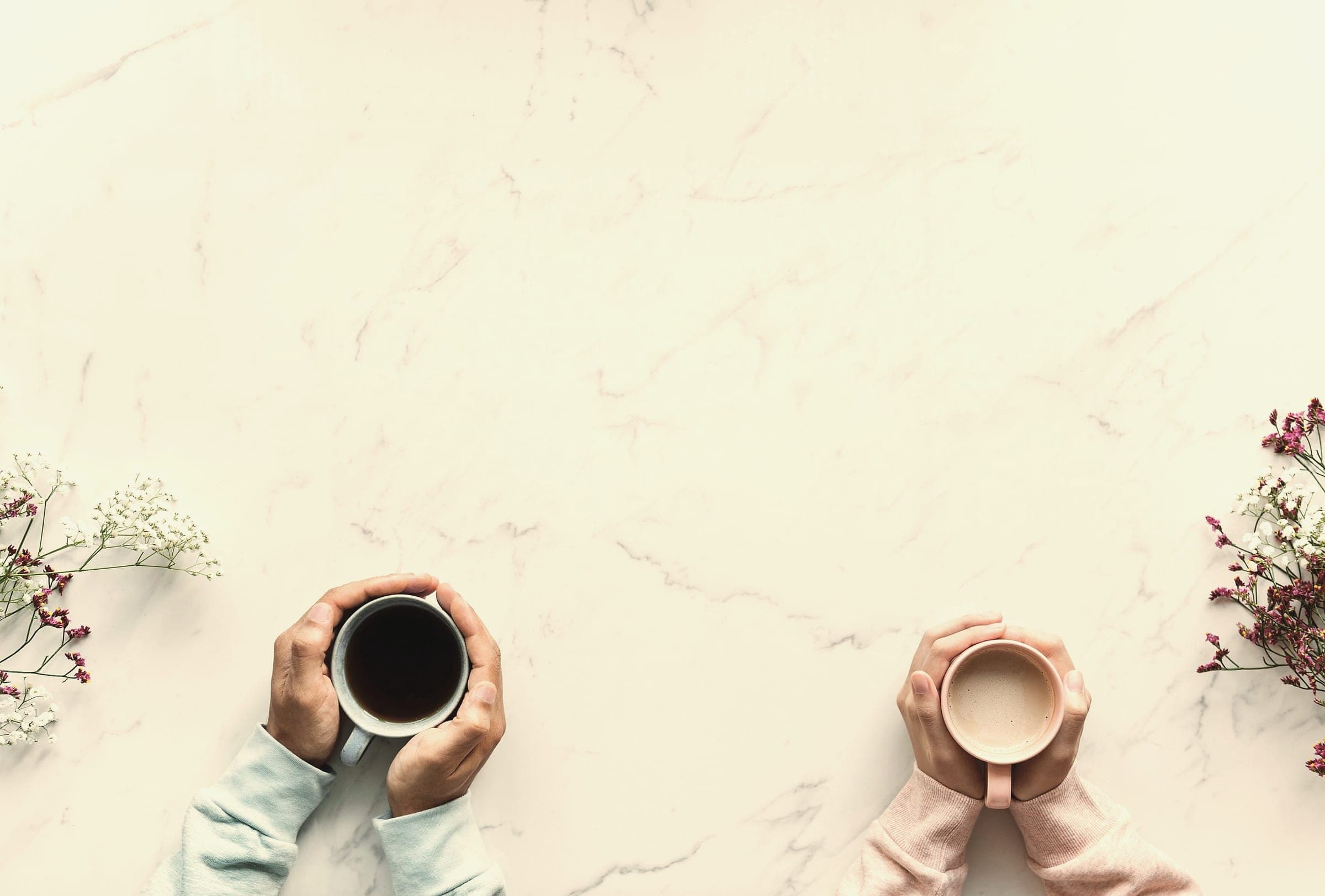 Two people sit across a table from one another, each holding a warm mug.